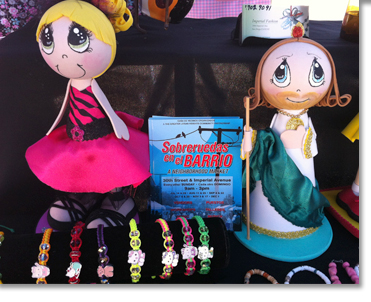In the booth next door, two local artisan-made dolls stand besides Casas de Vecinos Organizados fliers for the Sobreruedas.